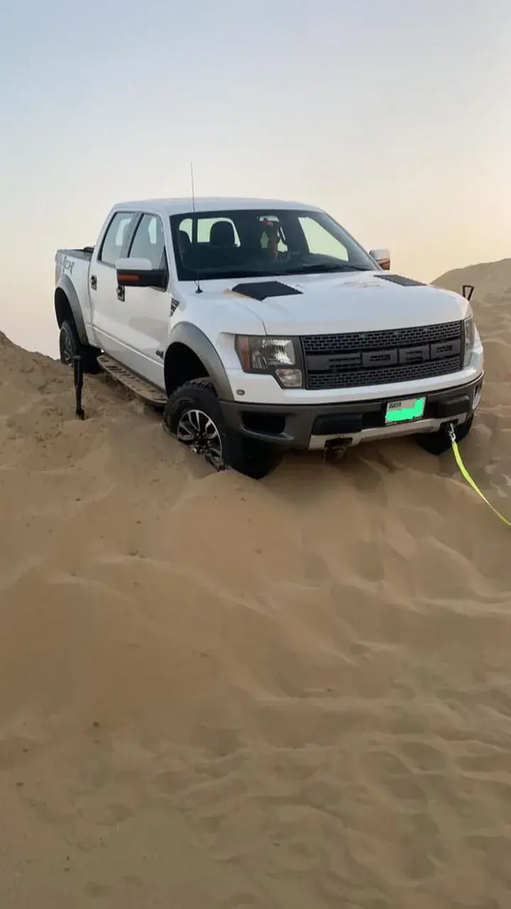 White pickup truck sunk into soft sand on a dune with a yellow recovery strap on the sand